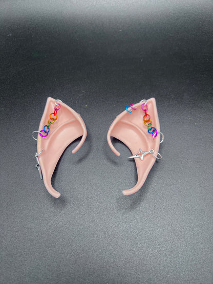 fantasy fairy elf ears with rainbow chain going across and star earrings. Left ear has 2 extra loop piercings in pink and blue
