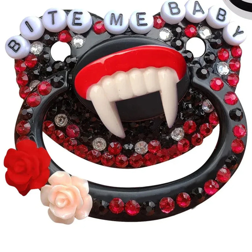 A black adult pacifier adorned with black and red gems, featuring fangs in the center and the text "Bite Me Baby" elegantly displayed along the top, creating a bold and edgy design.