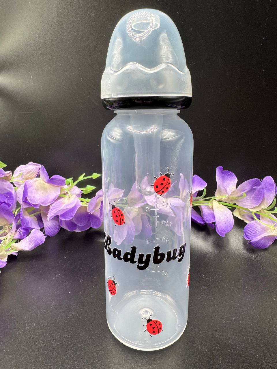 Clear ABDL bottle with ladybug design on a black background with purple flowers
