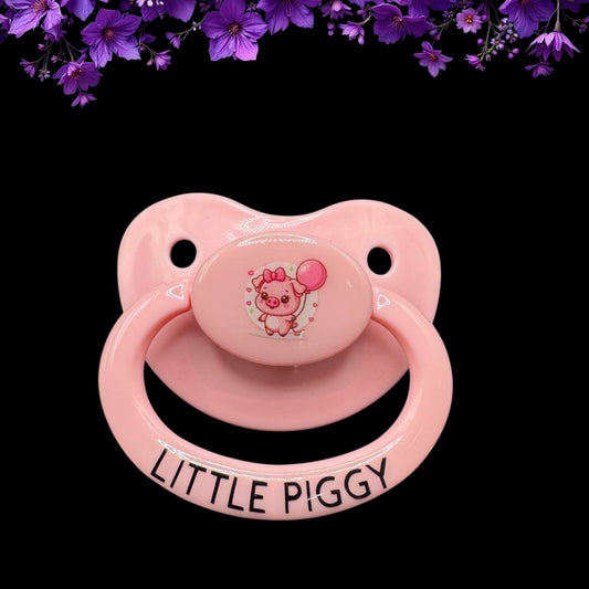 A pink adult pacifier with a cute pig graphic and the phrase 'LITTLE PIGGY' on it.