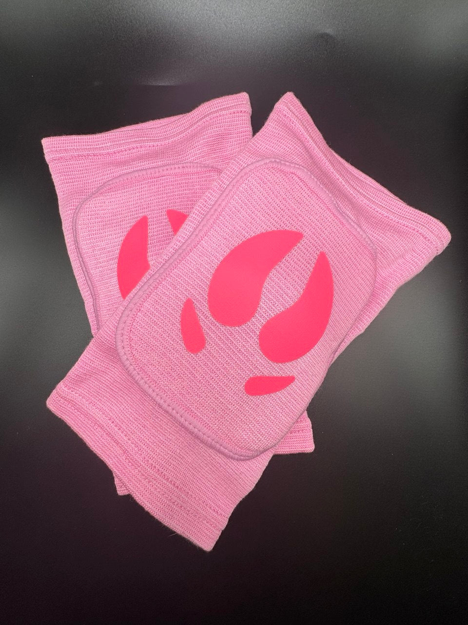 A pair of light pink ribbed knit knee pads with a darker pink pig hoof printed on the front