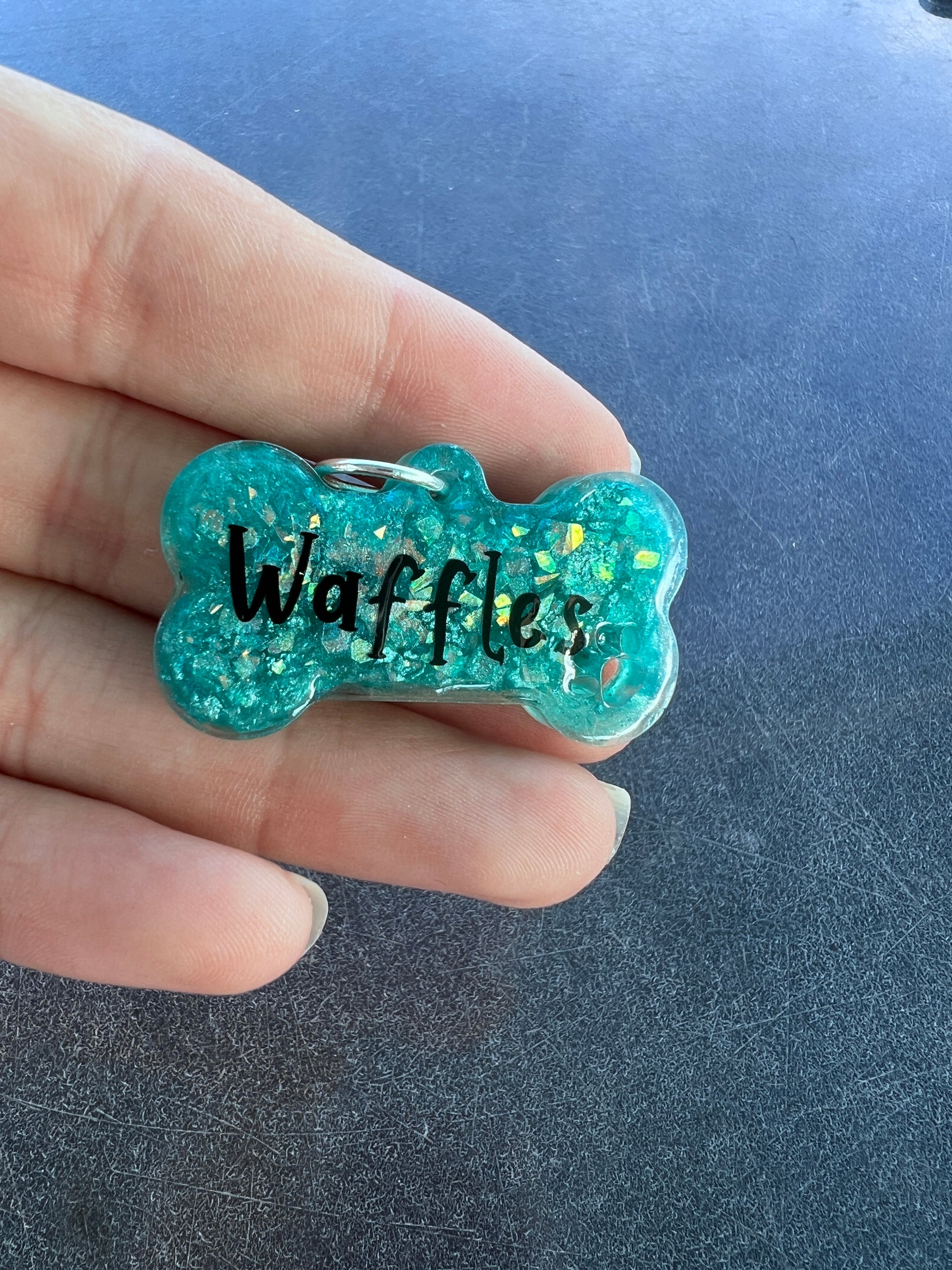 A vibrant teal bone-shaped resin pet play tag with the name 'Waffles' written in bold black text across the center.