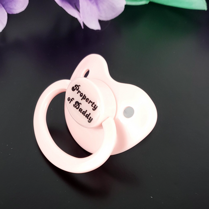 Baby Pink adult pacifier with bold text saying "Property of Daddy" in the center, adding a playful and loving sentiment. 