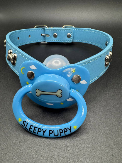 Blue dog bone straps with pacifier attachment with text 'Sleepy Puppy' on a gray background