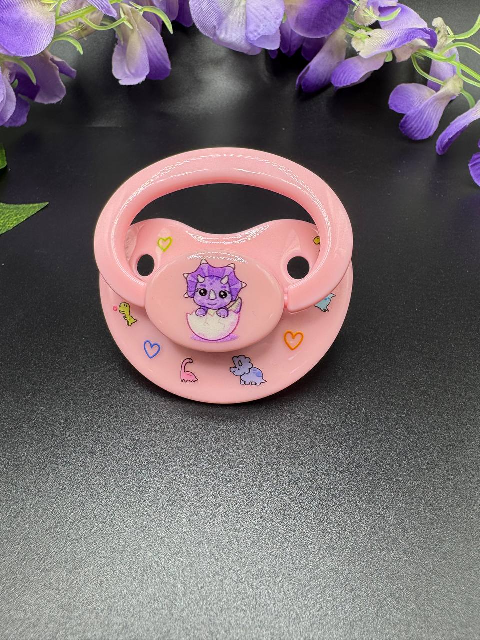 Purple triceratops image on pink ABDL adult pacifier with glow in the dark cute cartoon dinosaurs on the shield