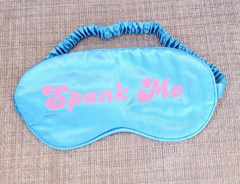 blue silk eye mask with pink text that says Spank Me