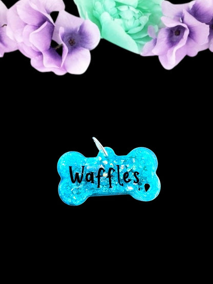 A vibrant teal bone-shaped resin pet play tag with the name 'Waffles' written in bold black text across the center.