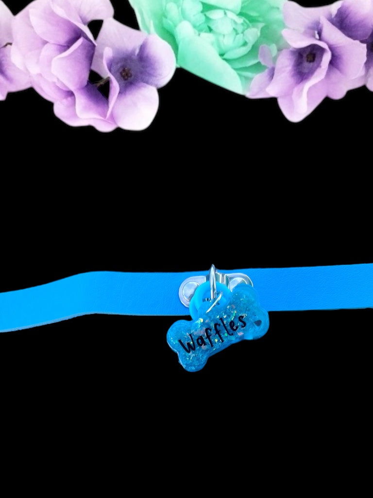 A vibrant teal bone-shaped resin pet play tag with the name 'Waffles' written in bold black text across the center.