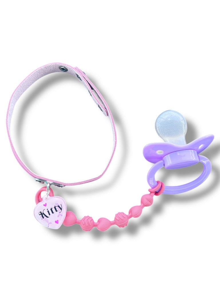 Baby pink adult choker with light pink resin tag that says Kitty attached to pink pacifier chewable string and lavender adult pacifier