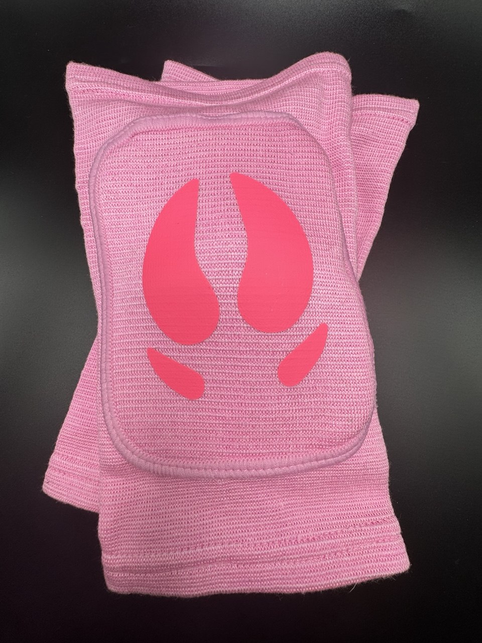 A pair of pink knit knee pads with a bright pink animal hooves design on the front, displayed against a dark background.