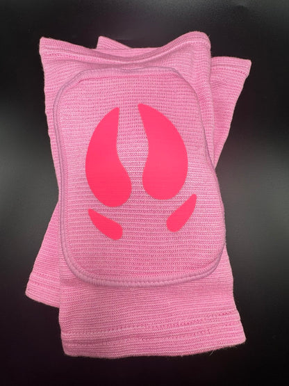 A pair of pink knit knee pads with a bright pink animal hooves design on the front, displayed against a dark background.