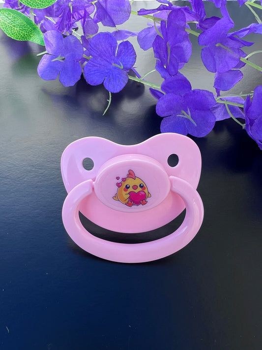 Adult pacifier featuring a cute baby chicken holding a heart with hearts flying away