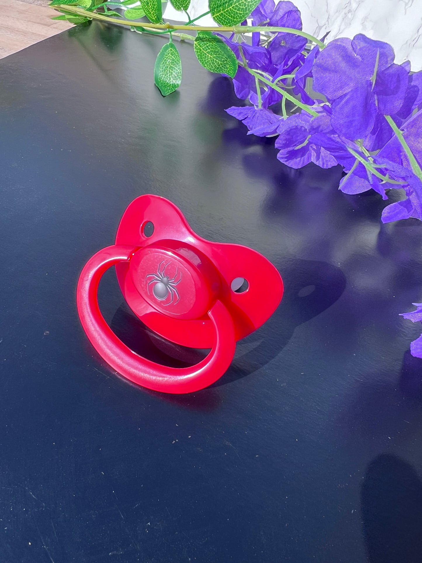red adult pacifier with black spider image in the center