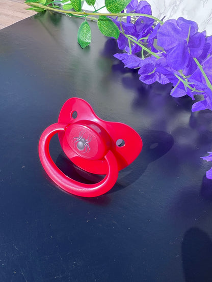 red adult pacifier with black spider image in the center