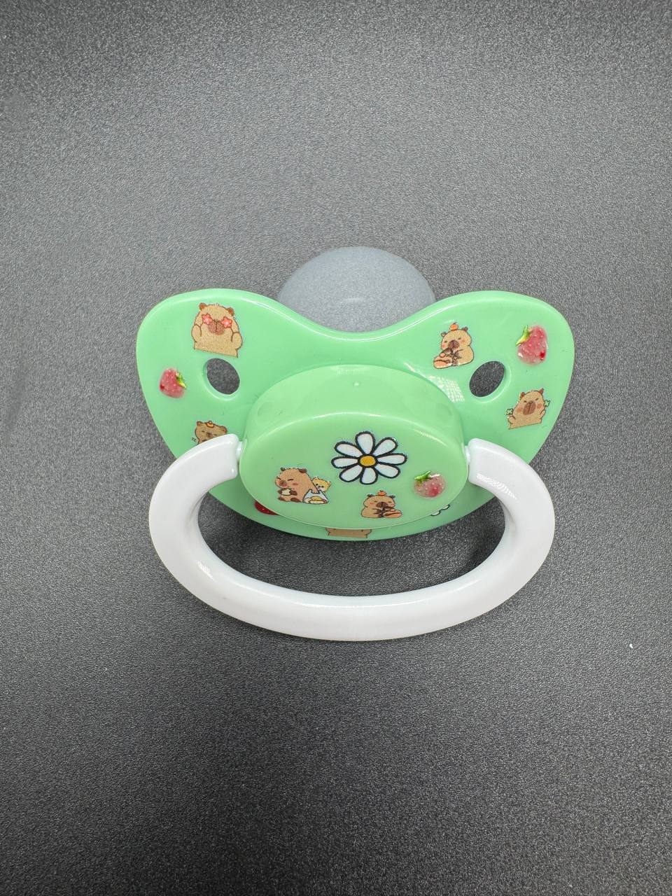 Green adult pacifier with cartoon designs on a gray background