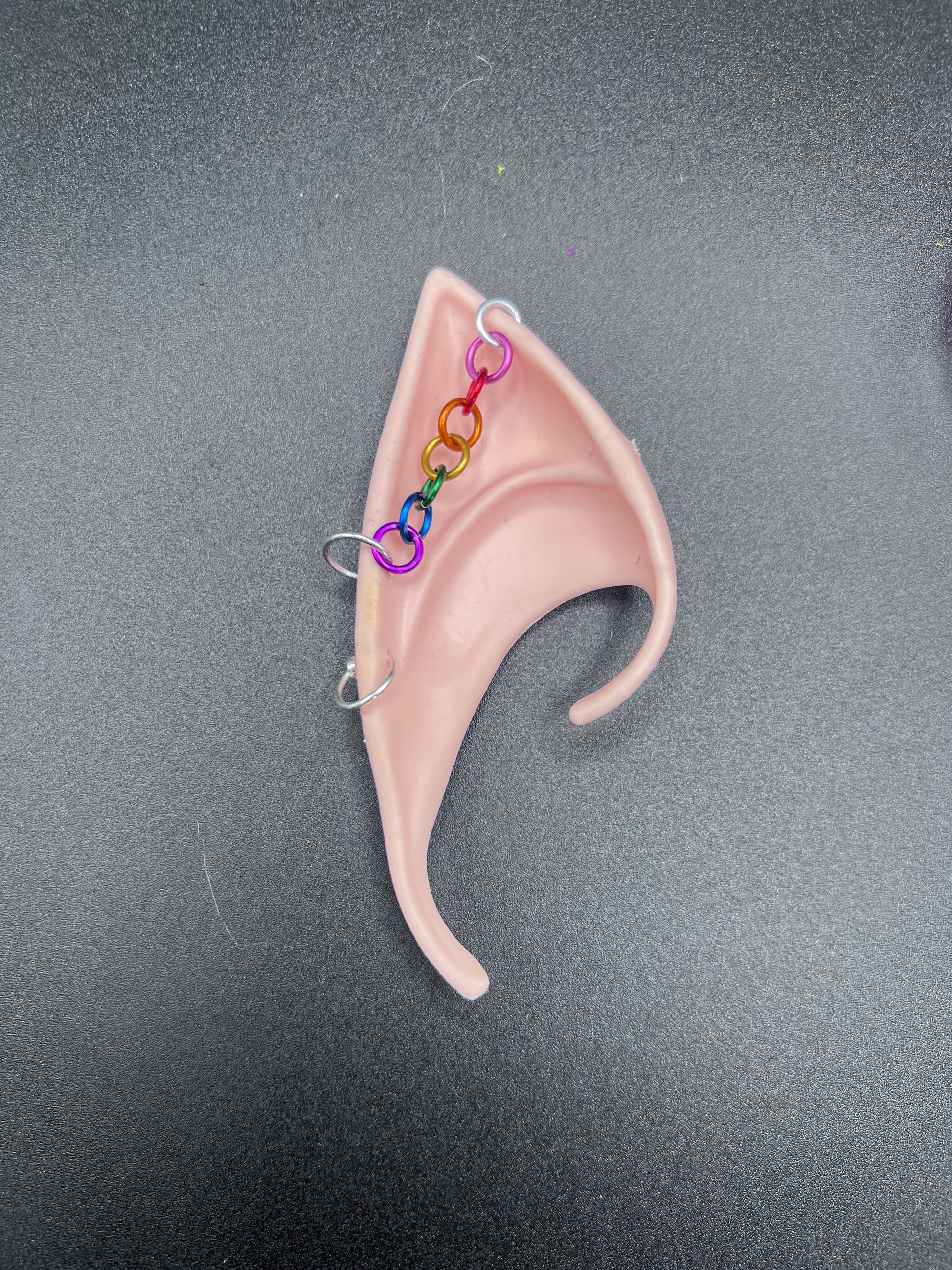 Tan elf ear with rainbow chain on a gray background