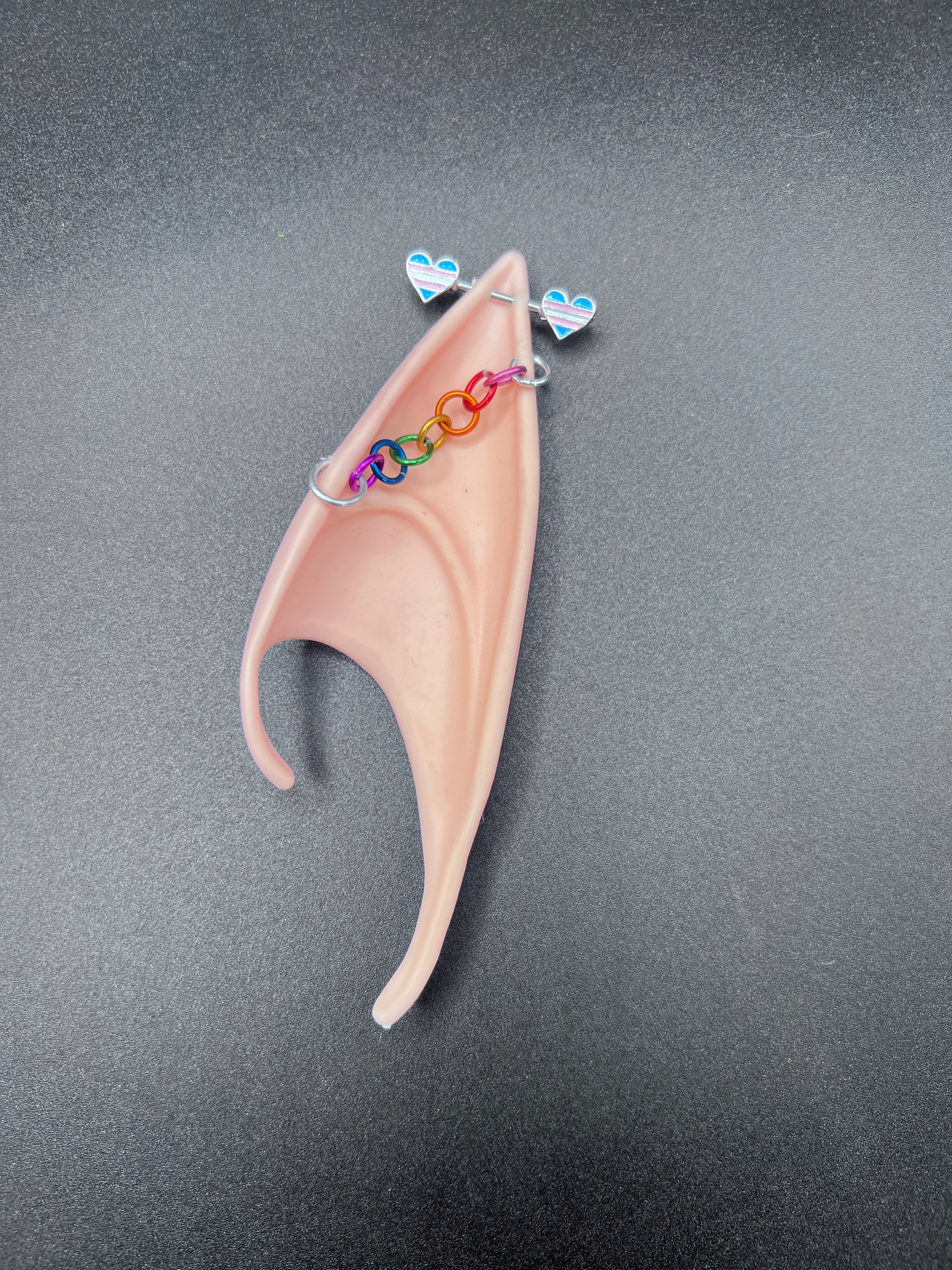 Artificial costume ear with colorful earrings on a gray background