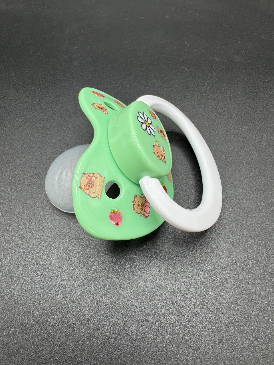Green adult binkie pacifier with floral and capybara designs on a gray background