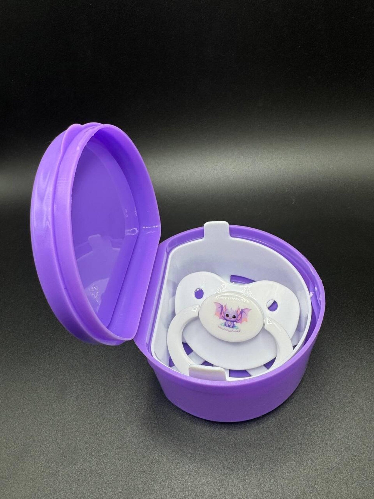 Purple pacifier case with a white bat themed adult pacifier inside 