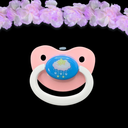 Adult dummy pacifier in baby pink, baby blue and baby white with center image of kawaii star sitting on a cloud with dangling hearts and stars like a mobile