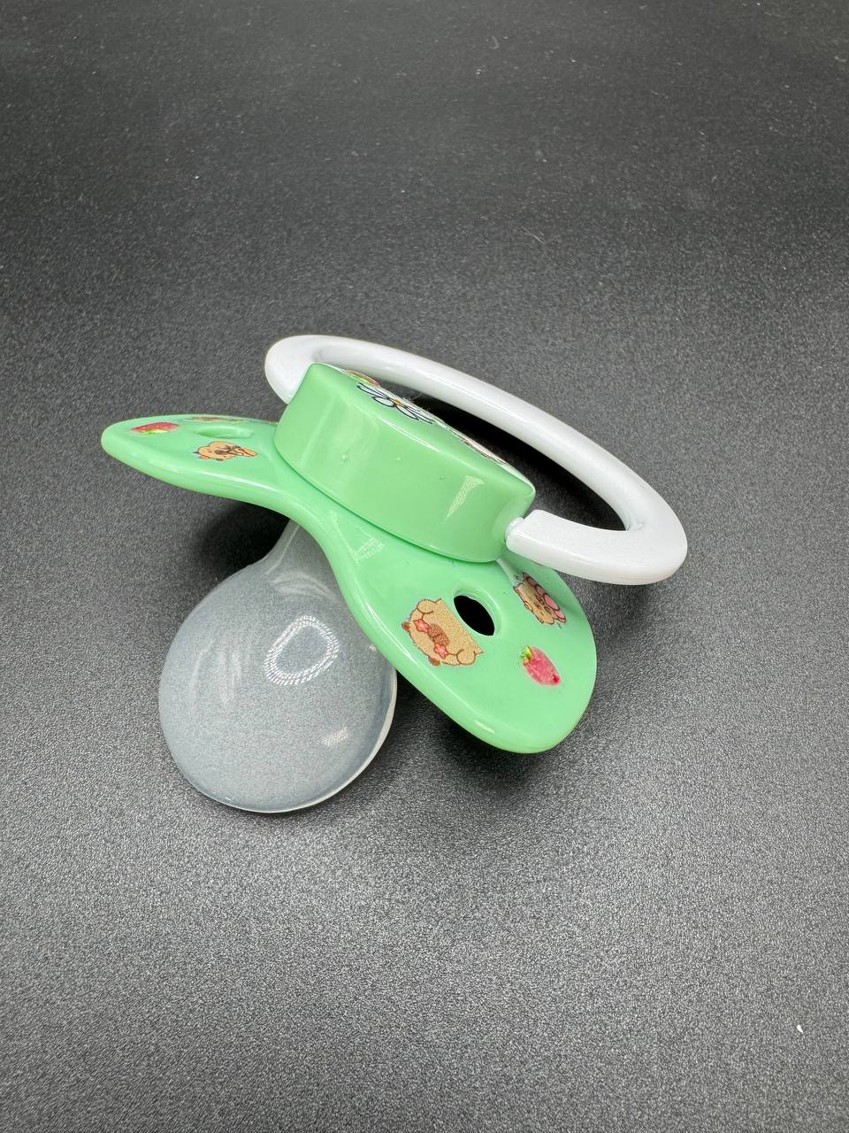 Mint pacifier with a white handle on a dark surface