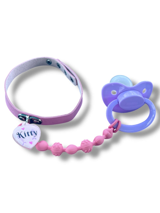 A pink adult pacifier choker with a silicone strand and a kitty tag, designed for comfort and style.