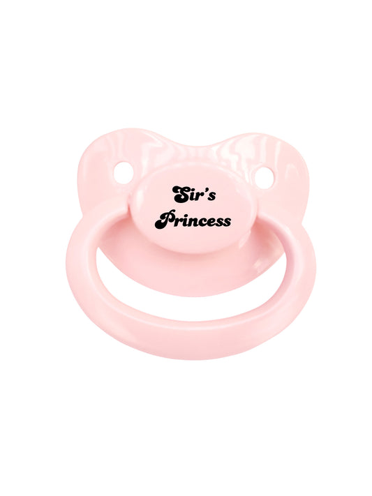 A pink adult pacifier with the phrase 'Sir's Princess' printed on the button.