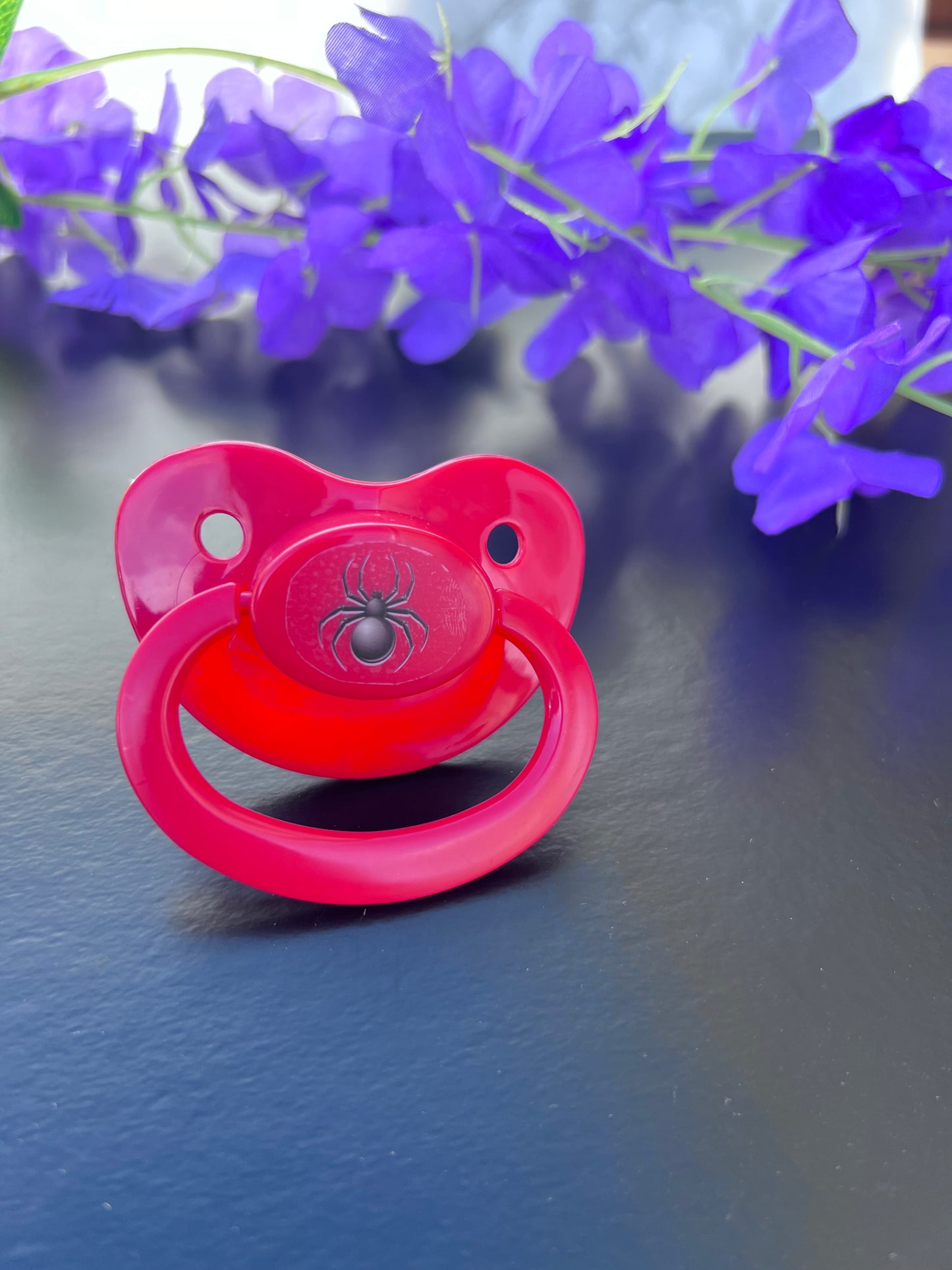 red adult pacifier with black spider on the center