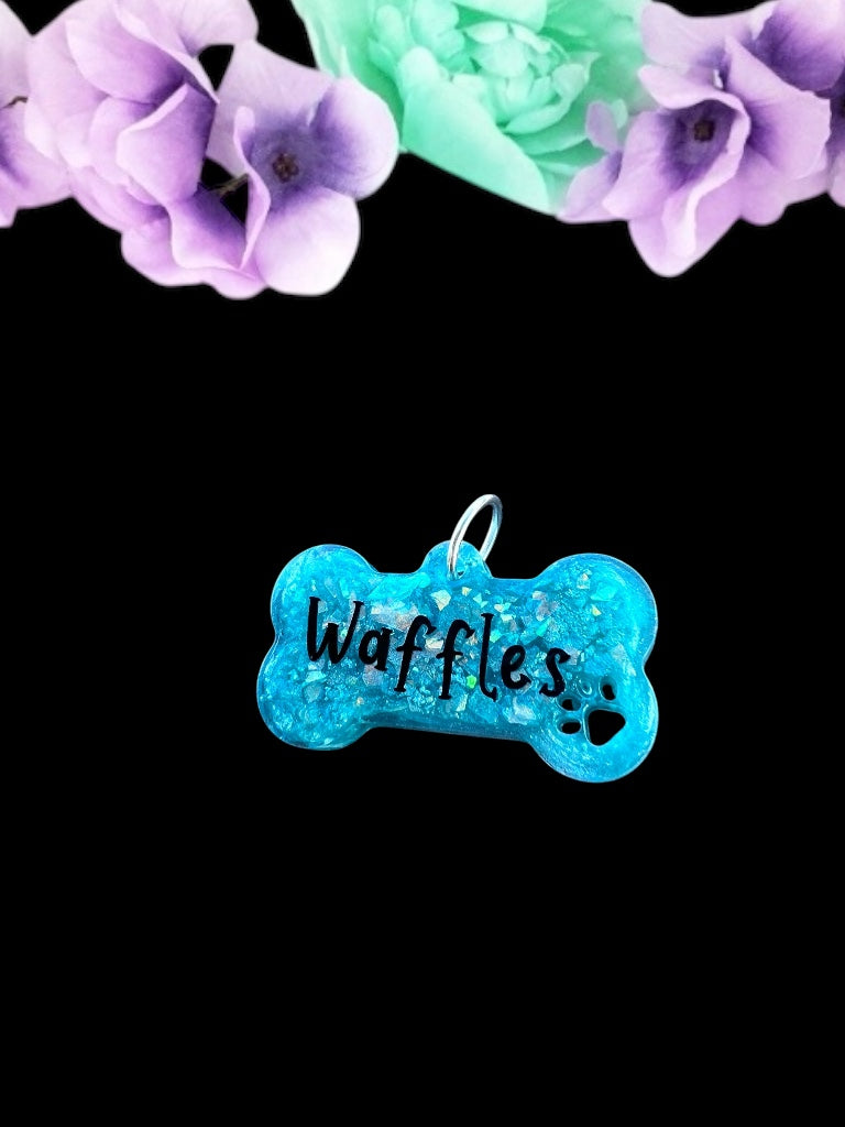 A vibrant teal bone-shaped resin pet play tag with the name 'Waffles' written in bold black text across the center.