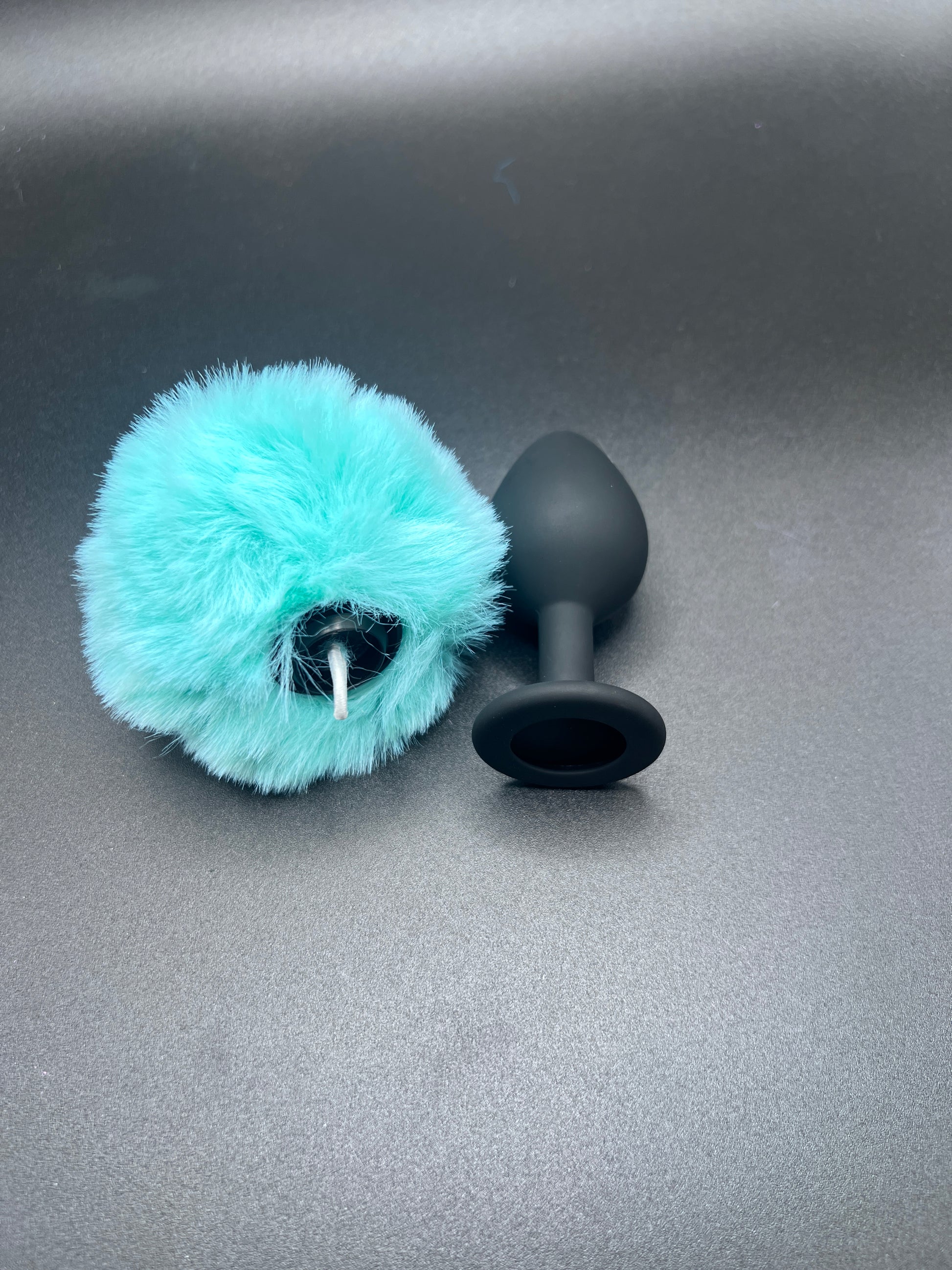 Black butt plug with a turquoise fuzzy bunny tail detached on a gray background