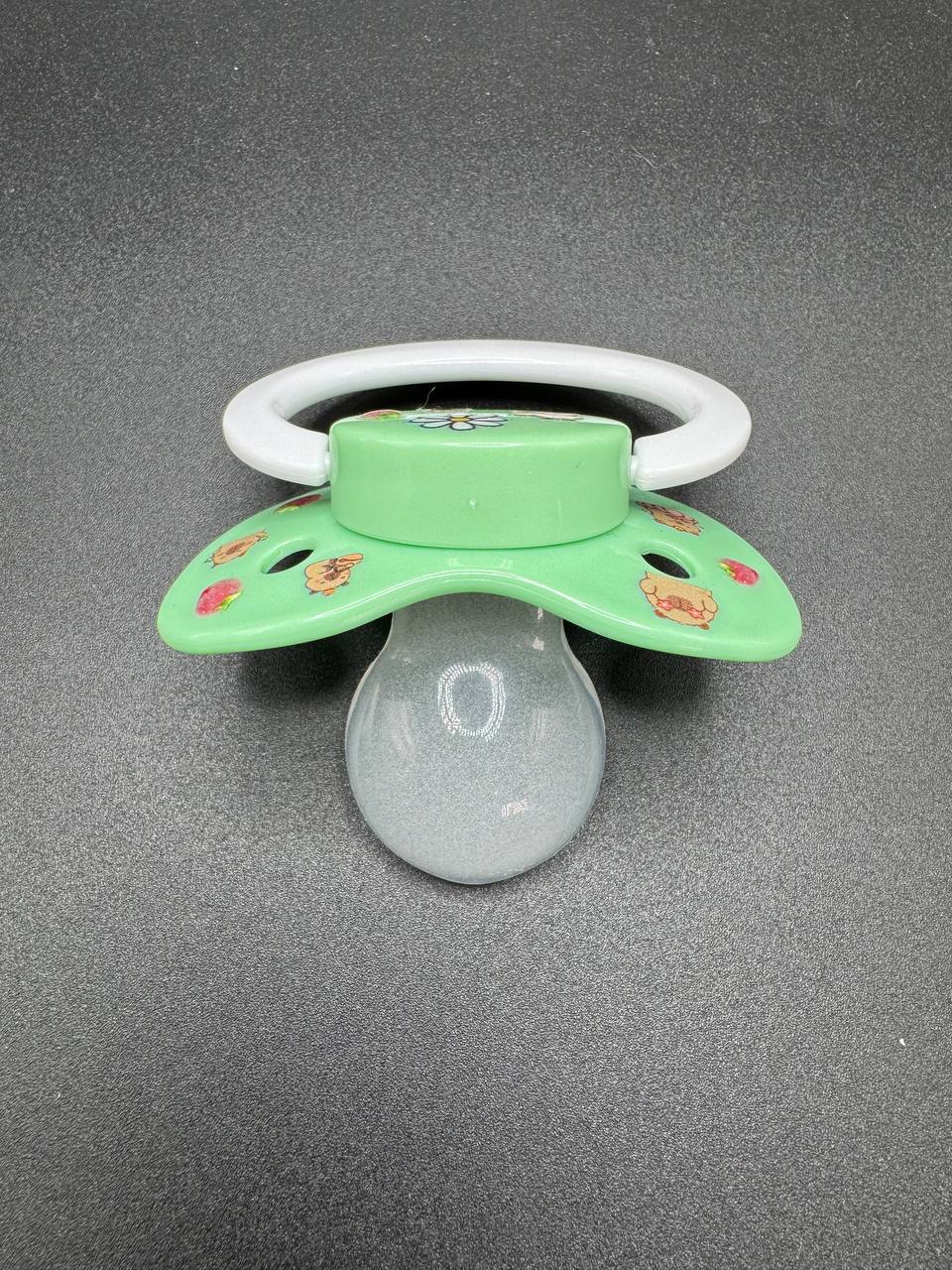 Green adult pacifier with white ring on a gray background