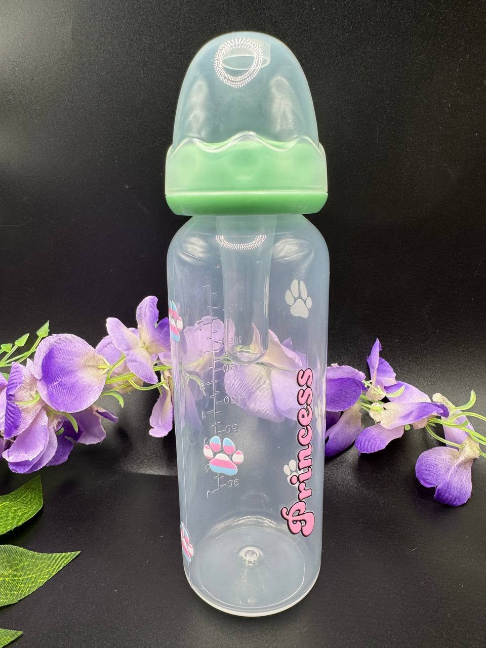 Clear adult baby bottle with green cap and 'Princess' text with paw prints in the color of trans pride flag