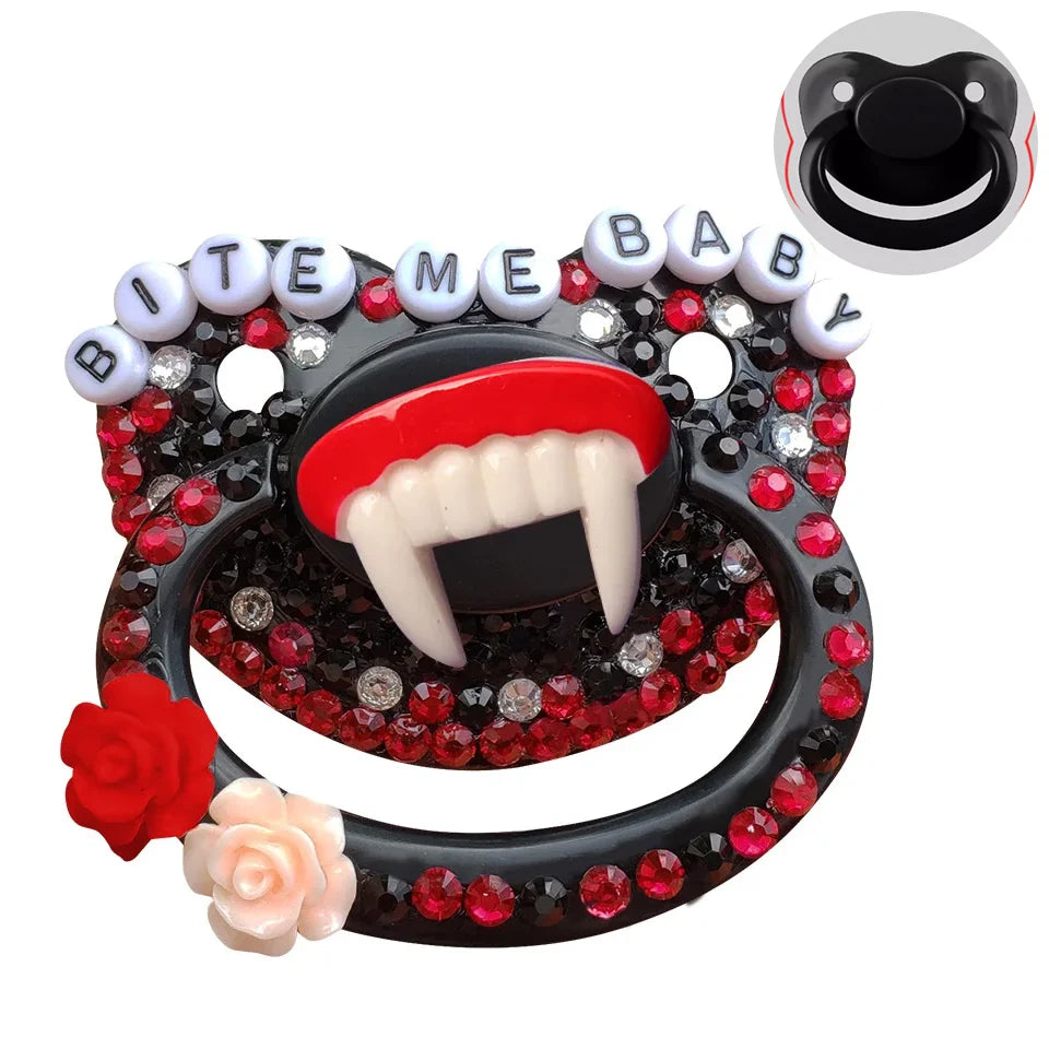 A black adult pacifier adorned with black and red gems, featuring fangs in the center and the text "Bite Me Baby" elegantly displayed along the top, creating a bold and edgy design.