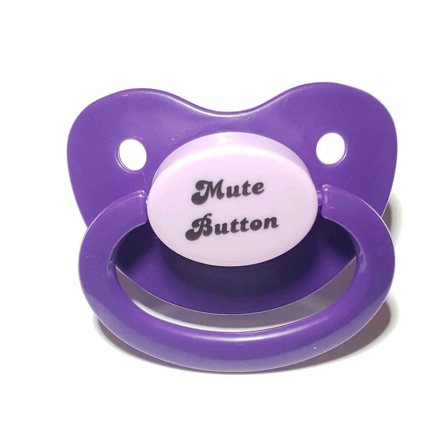 A purple adult pacifier with elegant black text in the center that reads "Mute Button," featuring a soft and playful design.