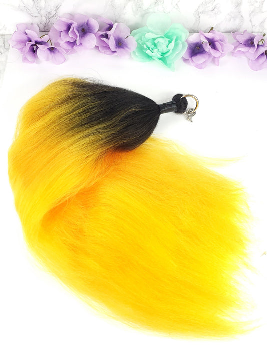 A synthetic yellow ombre pony tail with a black and yellow color gradient, featuring a D-ring attachment.