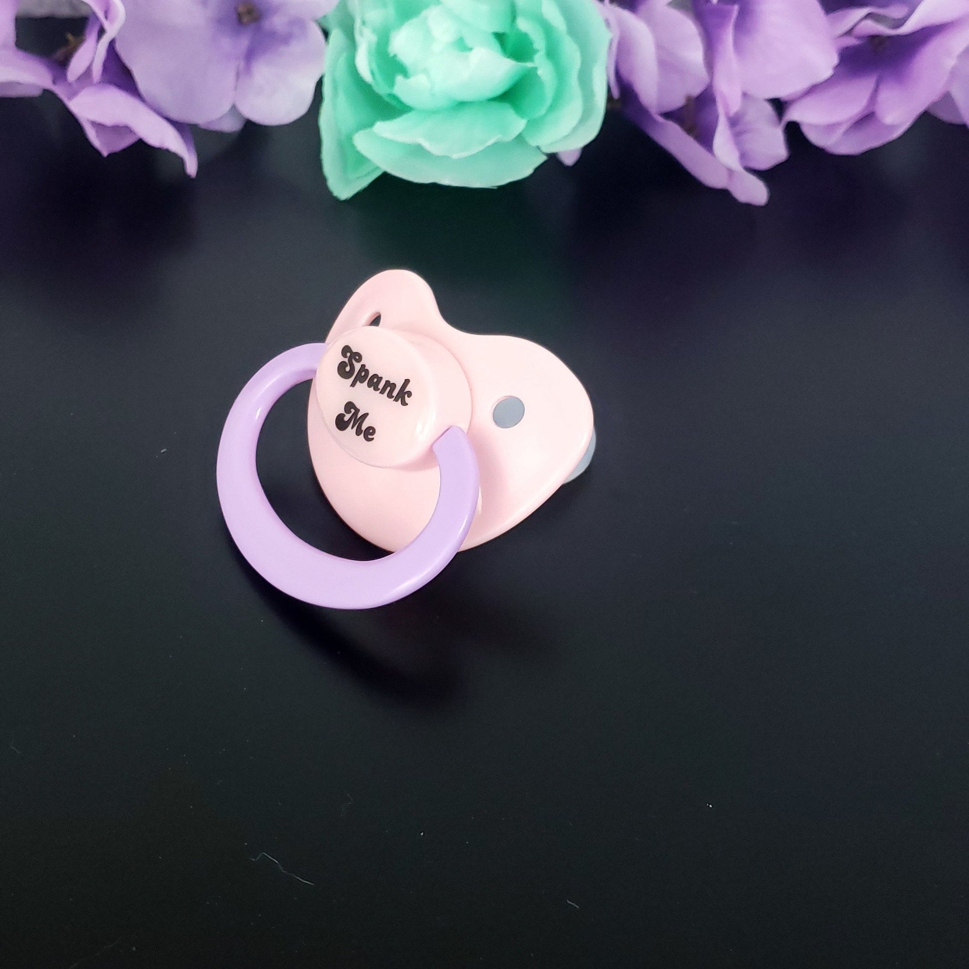 pastel adult pacifier with the text "Spank me" in the center