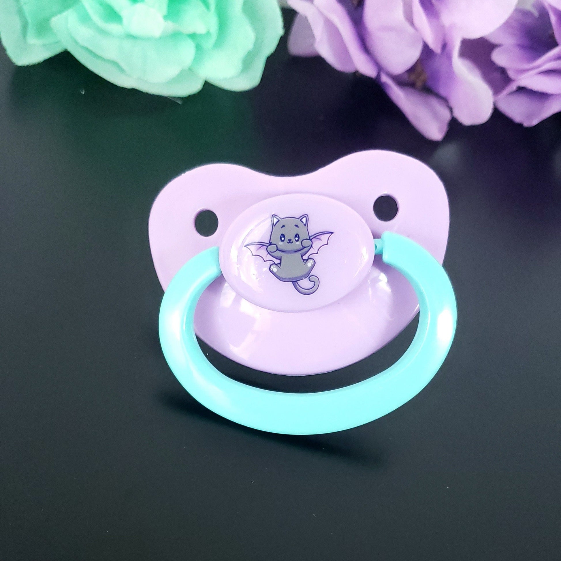 pastel purple adult pacifier with aqua handle featuring a fun and cute cat with bat wings