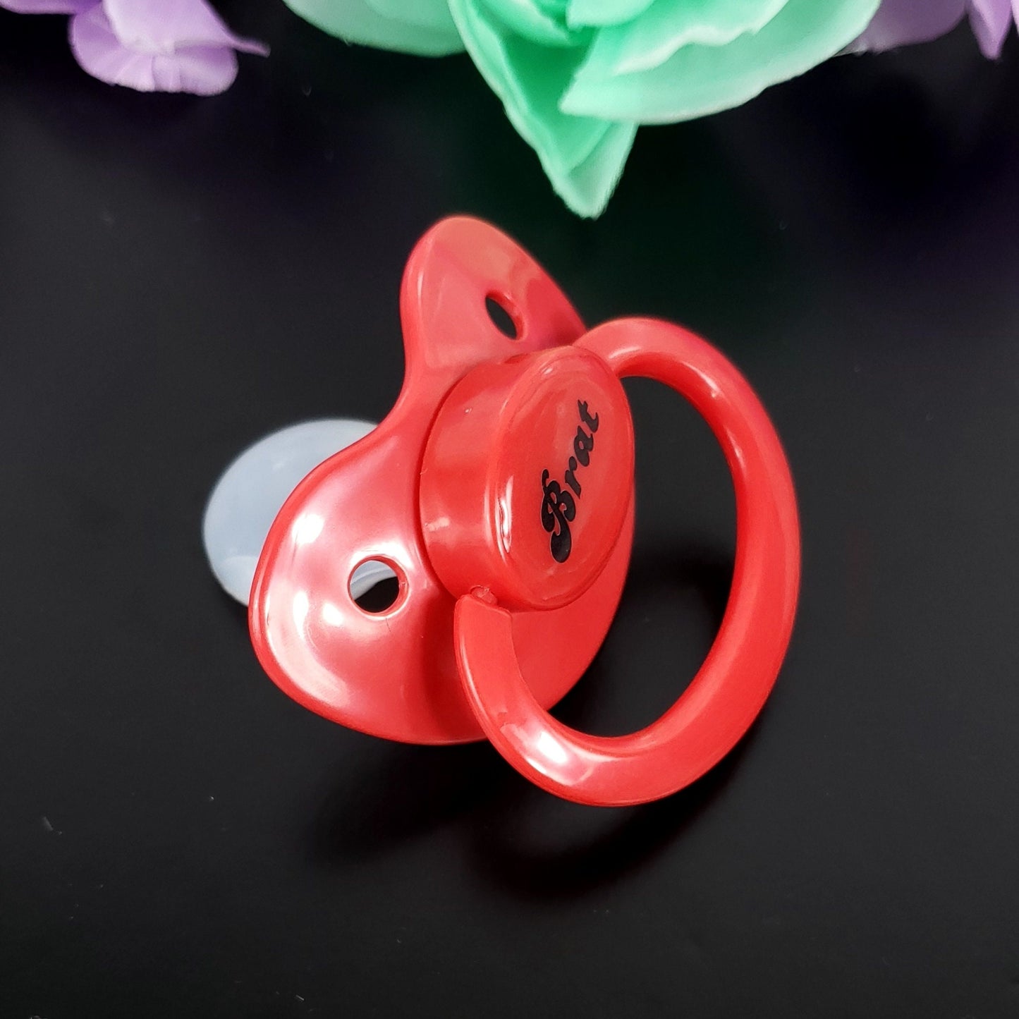 A red adult pacifier featuring the word "Brat" boldly displayed in the center, designed for playful and cheeky self-expression.