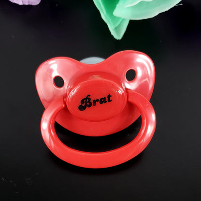 A red adult pacifier featuring the word "Brat" boldly displayed in the center, designed for playful and cheeky self-expression.