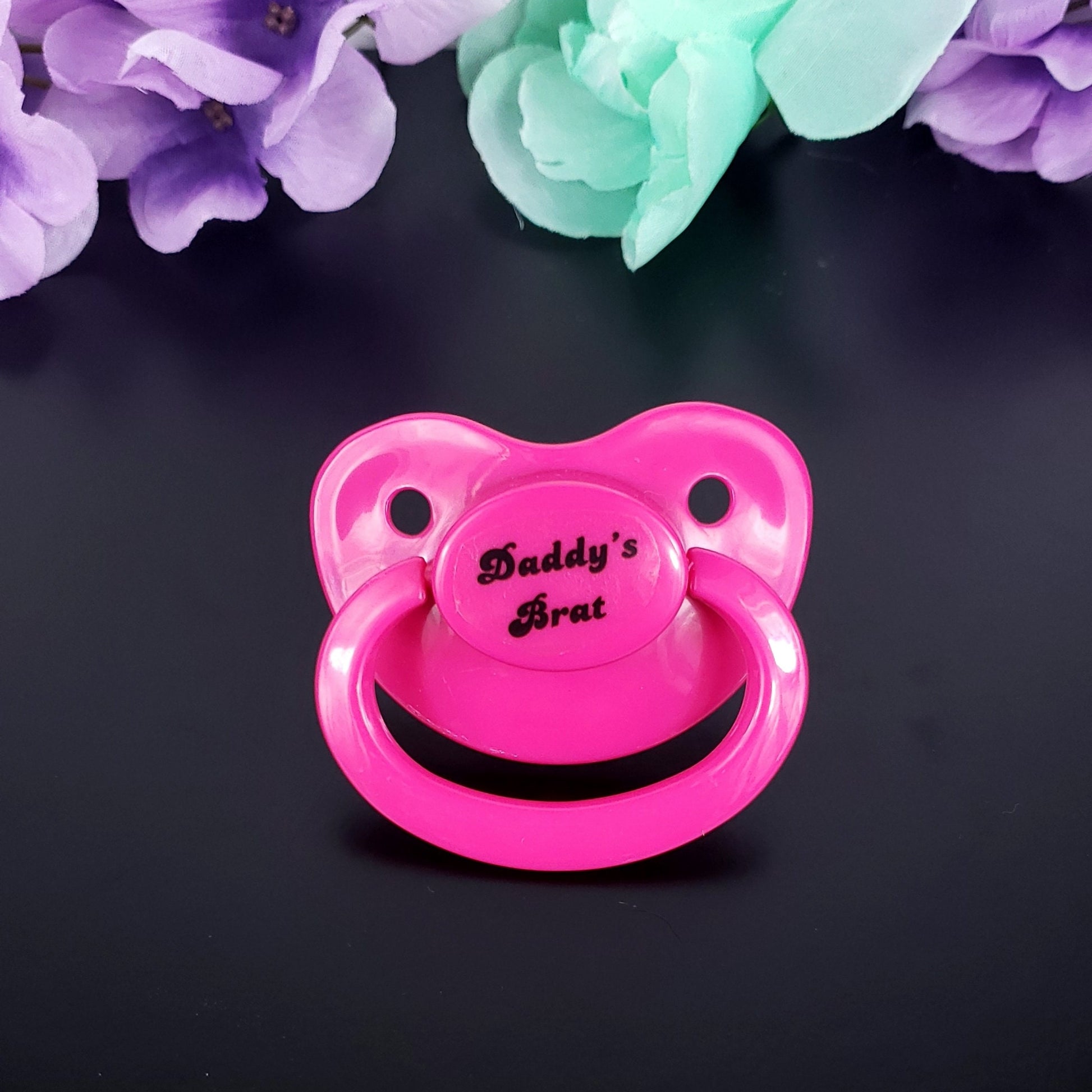 A hot pink adult pacifier featuring bold white text that reads "Daddy's Brat" in the center, showcasing a playful and sassy design.