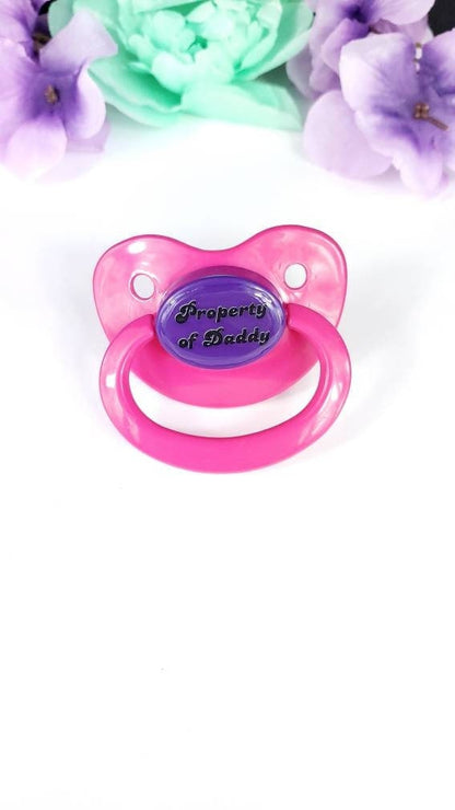 adult pacifier with bold text saying "Property of Daddy" in the center, adding a playful and loving sentiment. 