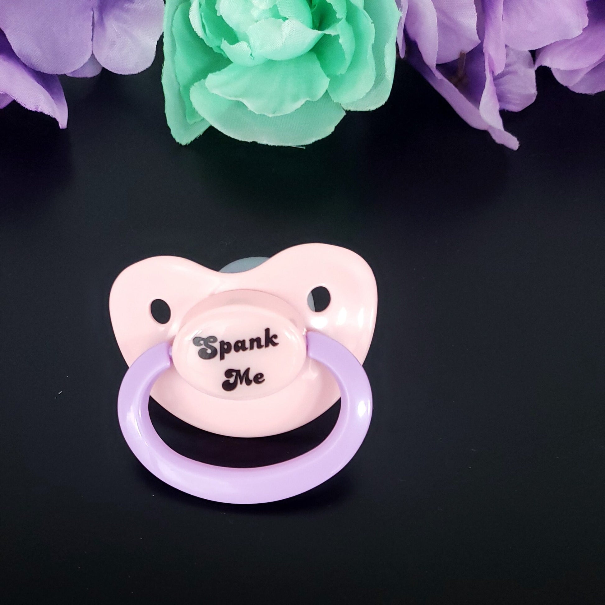 pastel adult pacifier with the text "Spank me" in the center