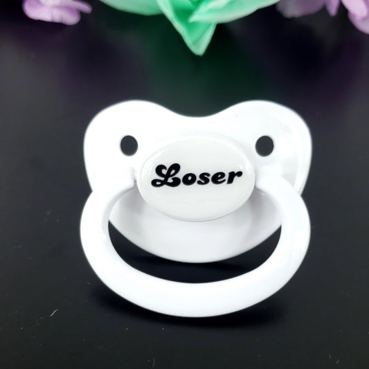 A white adult pacifier featuring bold black text in the center that reads "Loser," offering a simple and degrading design.