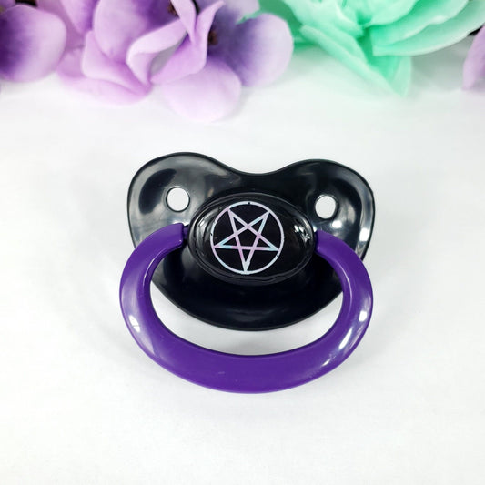 A black and purple adult pacifier with a pentagram design, displayed against a white background with floral patterns.