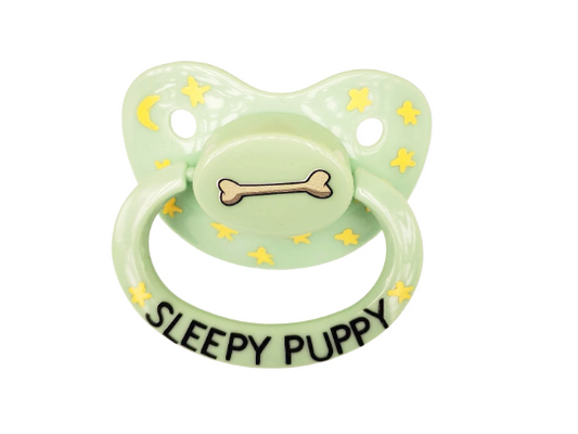 A green adult pacifier with yellow stars and a bone design, reading 'SLEEPY PUPPY' on the handle.