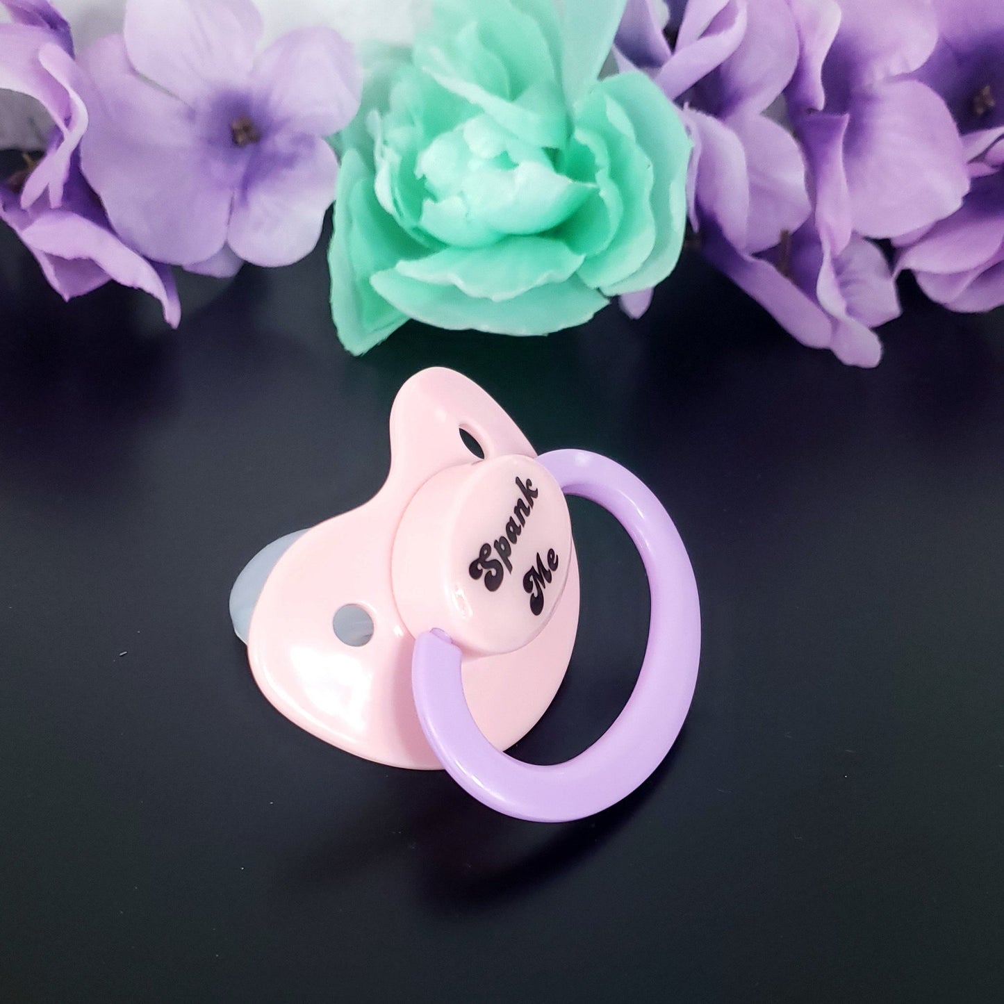 pastel adult pacifier with the text "Spank me" in the center