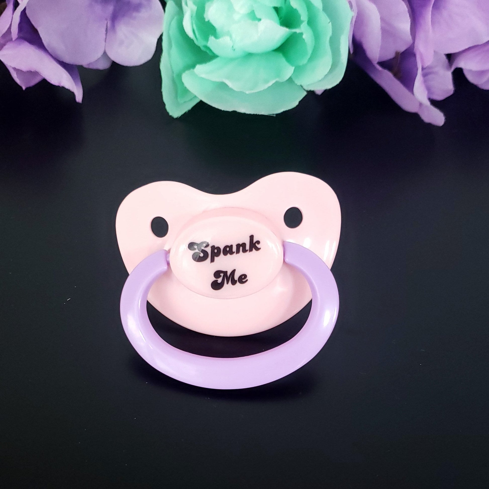 pastel adult pacifier with the text "Spank me" in the center